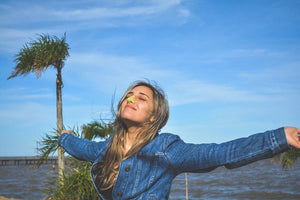 Woman wearing Nöz reef-safe sunscreen while embracing the sun with her arms out